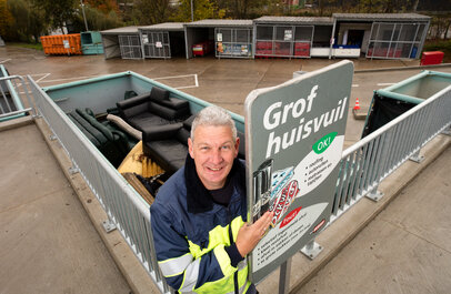 Man die voor de container grof huisvuil staat.