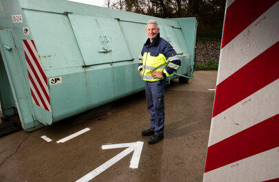 Man voor een afval container in het container park.
