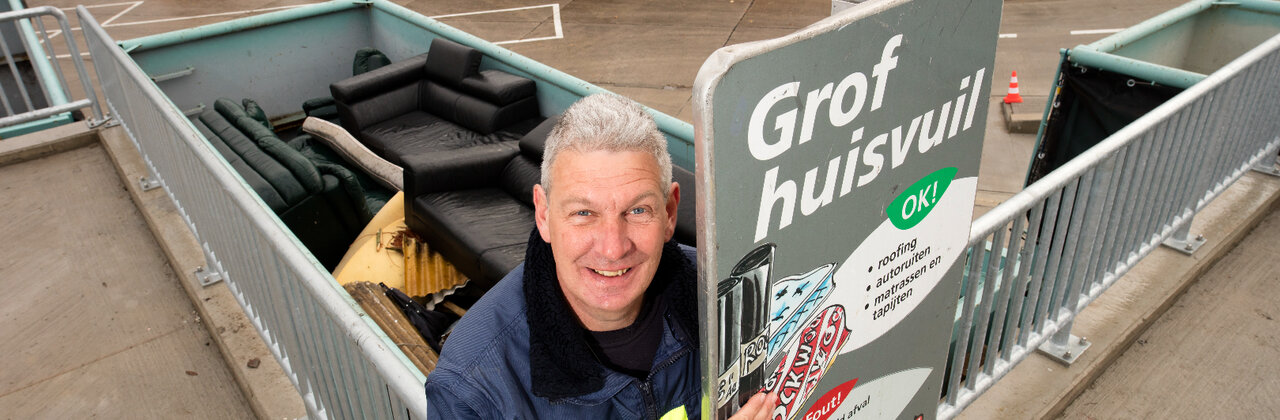 Man die voor de container grof huisvuil staat.