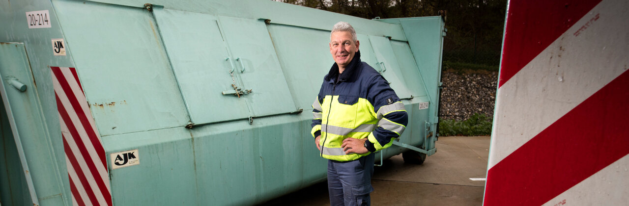 Man voor een afval container in het container park.