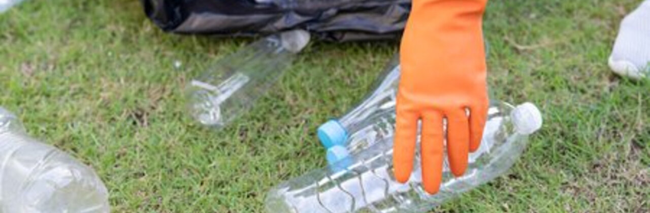 Persoon met handschoen die zwerfvuil opraapt.